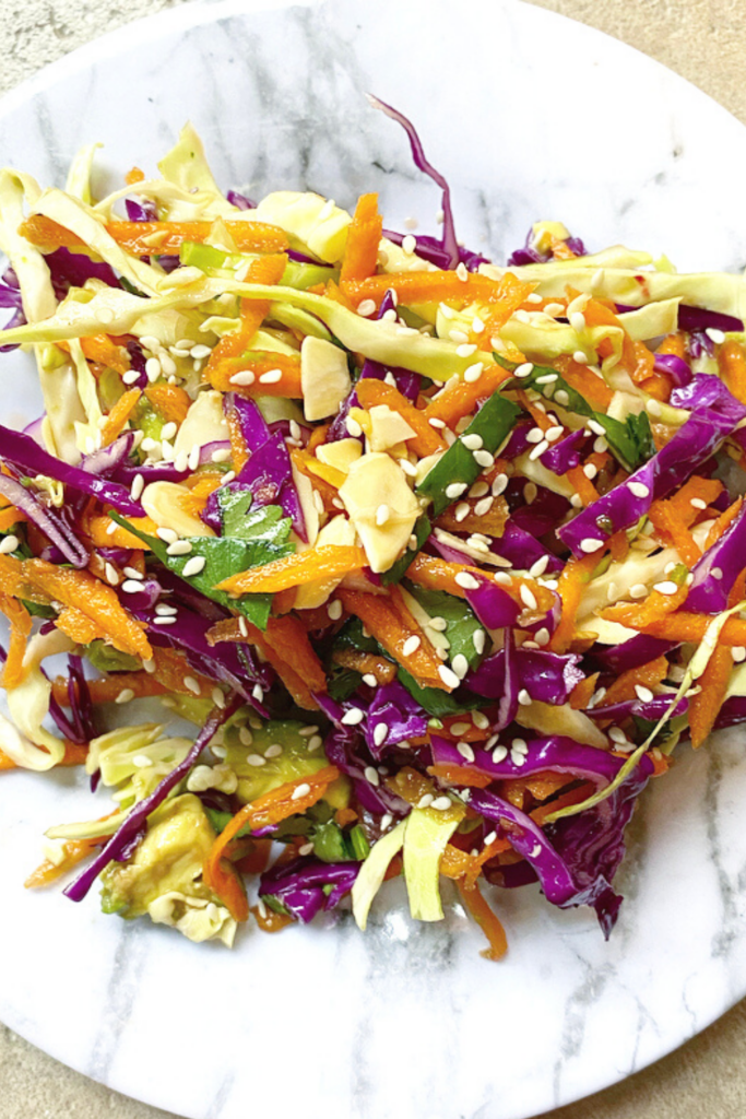 Asian spring salad filled with green and purple cabbage, oranges, cilantro, and almonds